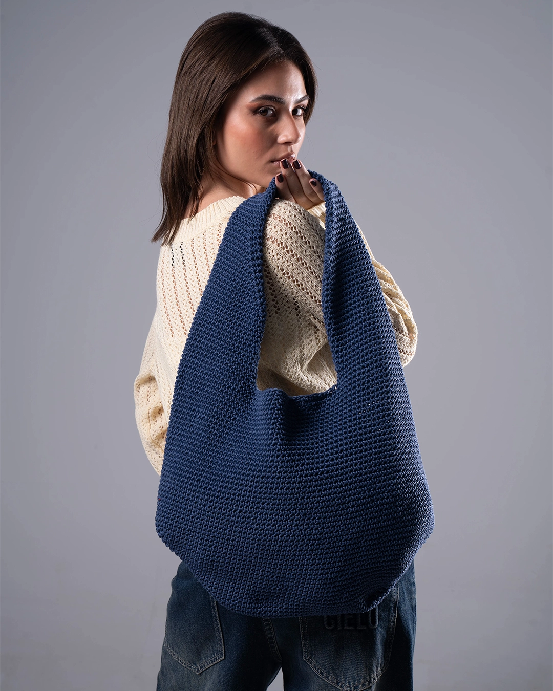 Woman holding a blue knitted bag against a gray background