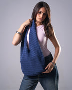Woman holding a blue crocheted bag against a gray background
