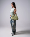 Woman holding a green woven handbag against a plain background