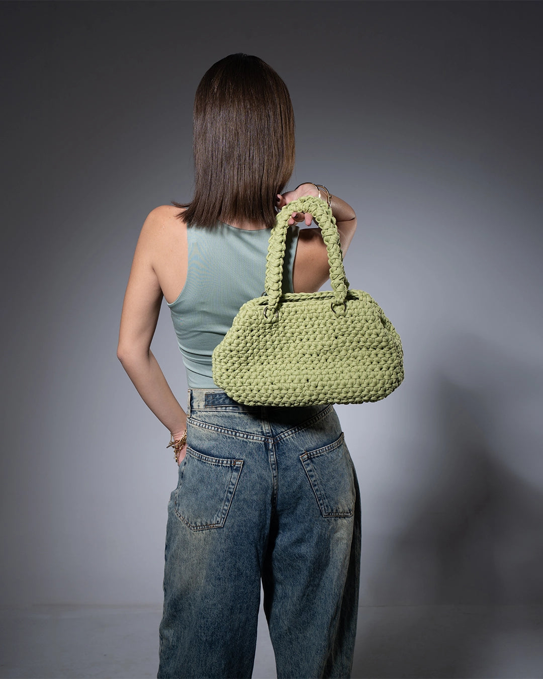 Person holding a green handbag against a gray background