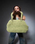 Woman holding a large green knitted bag against a dark background