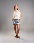 Woman wearing a white sleeveless top and denim shorts on a gray background