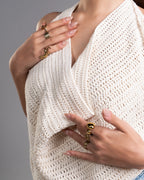 Close-up of a person wearing a white crochet top with gold jewelry on a gray background