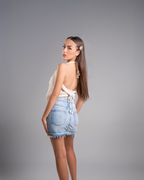Woman wearing a white top and denim shorts on a gray background