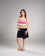 Woman wearing a colorful sleeveless top and black shorts on a gray background