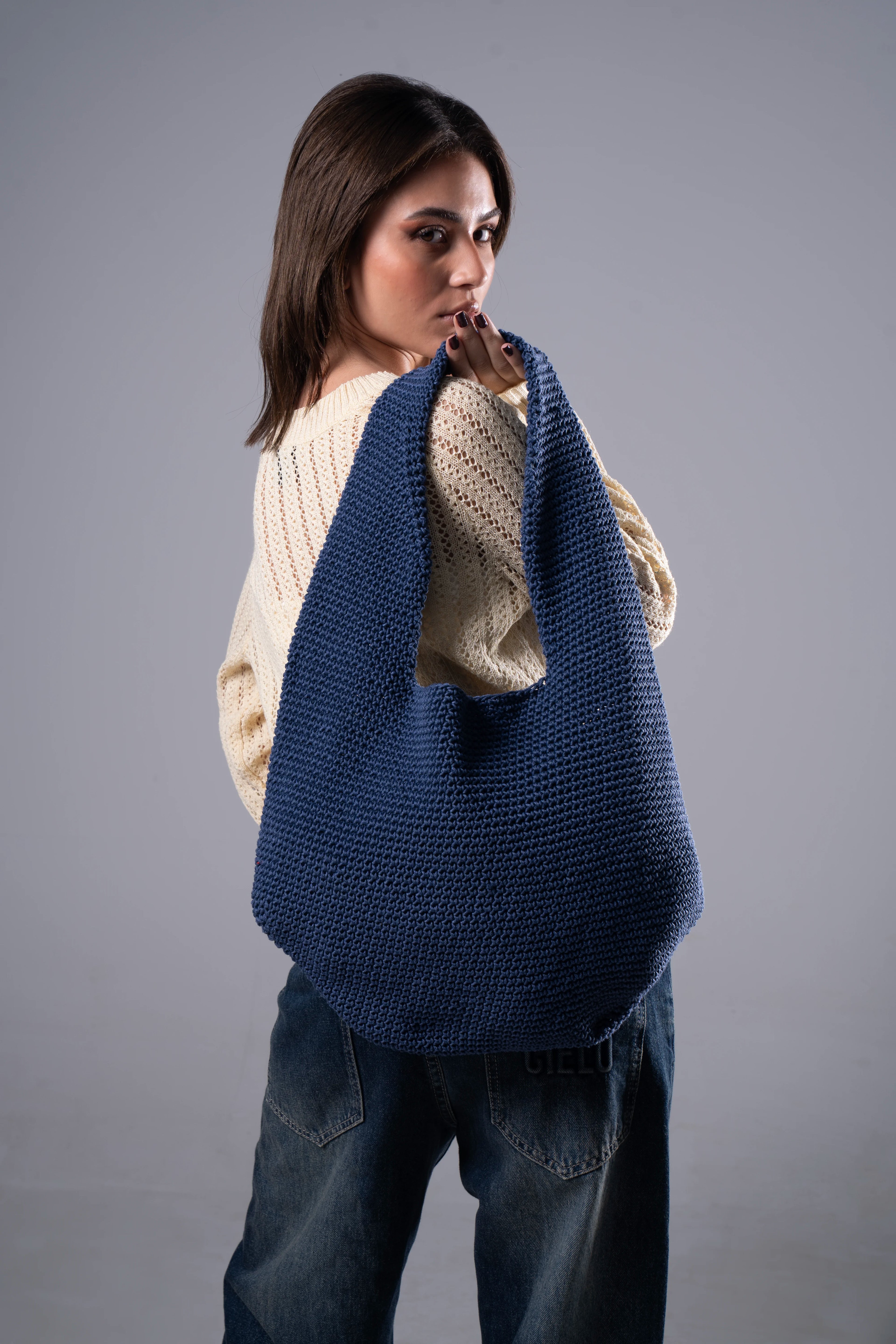 Woman holding a blue knitted bag against a gray background