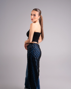 Woman wearing a black strapless top and dark blue patterned pants on a gray background
