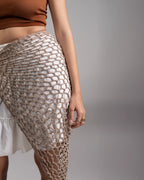 Person wearing a textured beige shawl over a white garment against a gray background