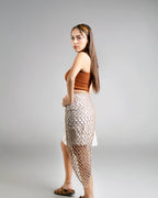 Woman wearing a brown top and fishnet skirt on a gray background