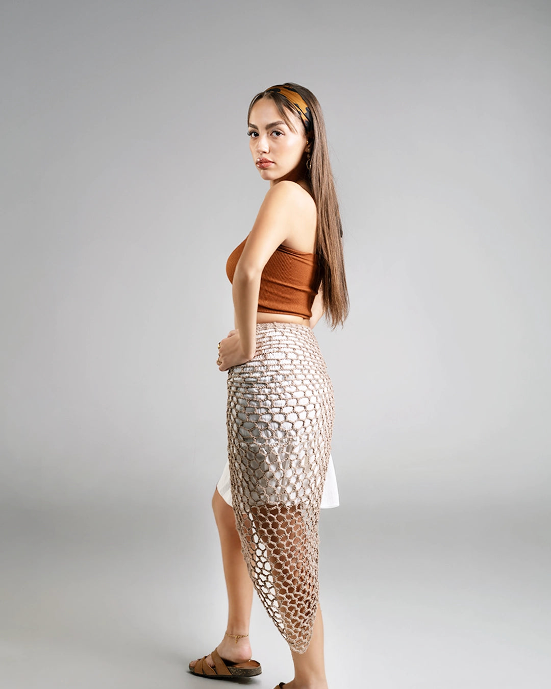 Woman wearing a brown top and fishnet skirt on a gray background