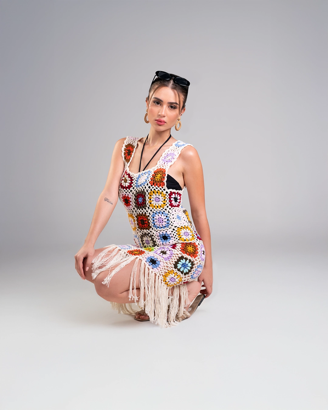 Woman wearing a colorful crochet dress with a pattern on a gray background