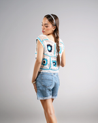 Woman wearing a colorful crochet top and denim shorts on a gray background
