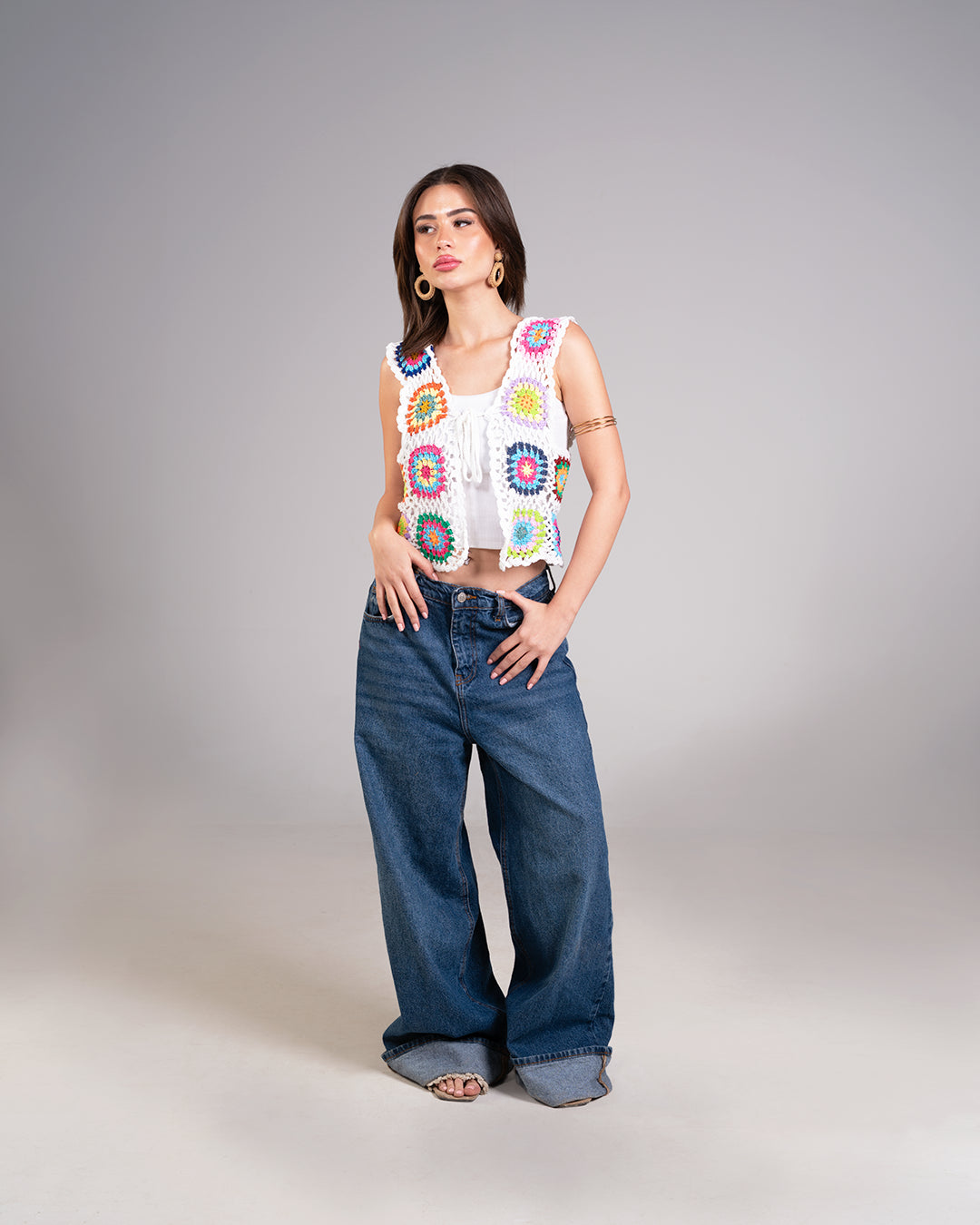 Woman wearing a colorful sleeveless top and blue jeans on a gray background
