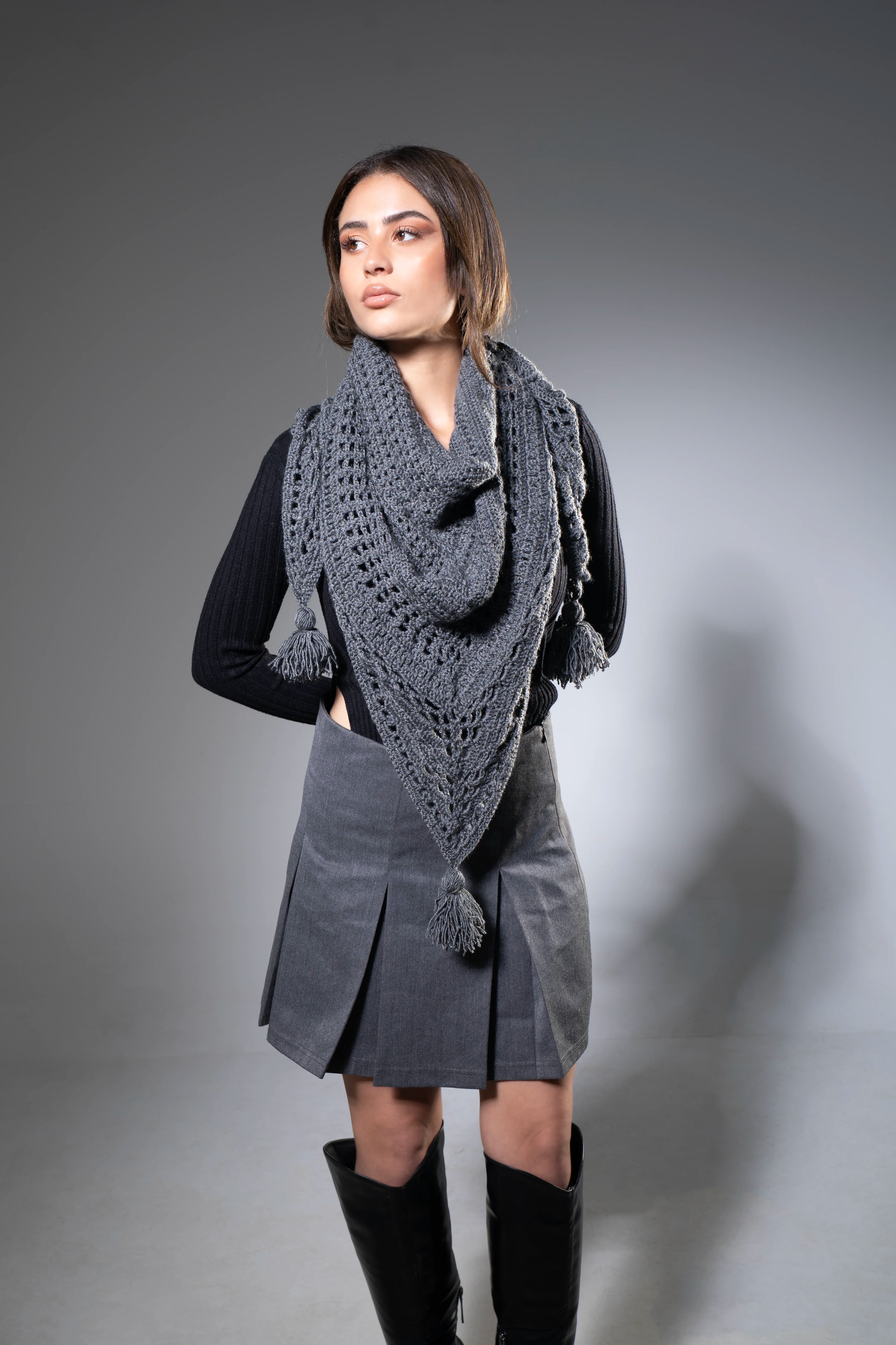 Woman wearing a dark gray knitted shawl over a black top and gray skirt on a gray background