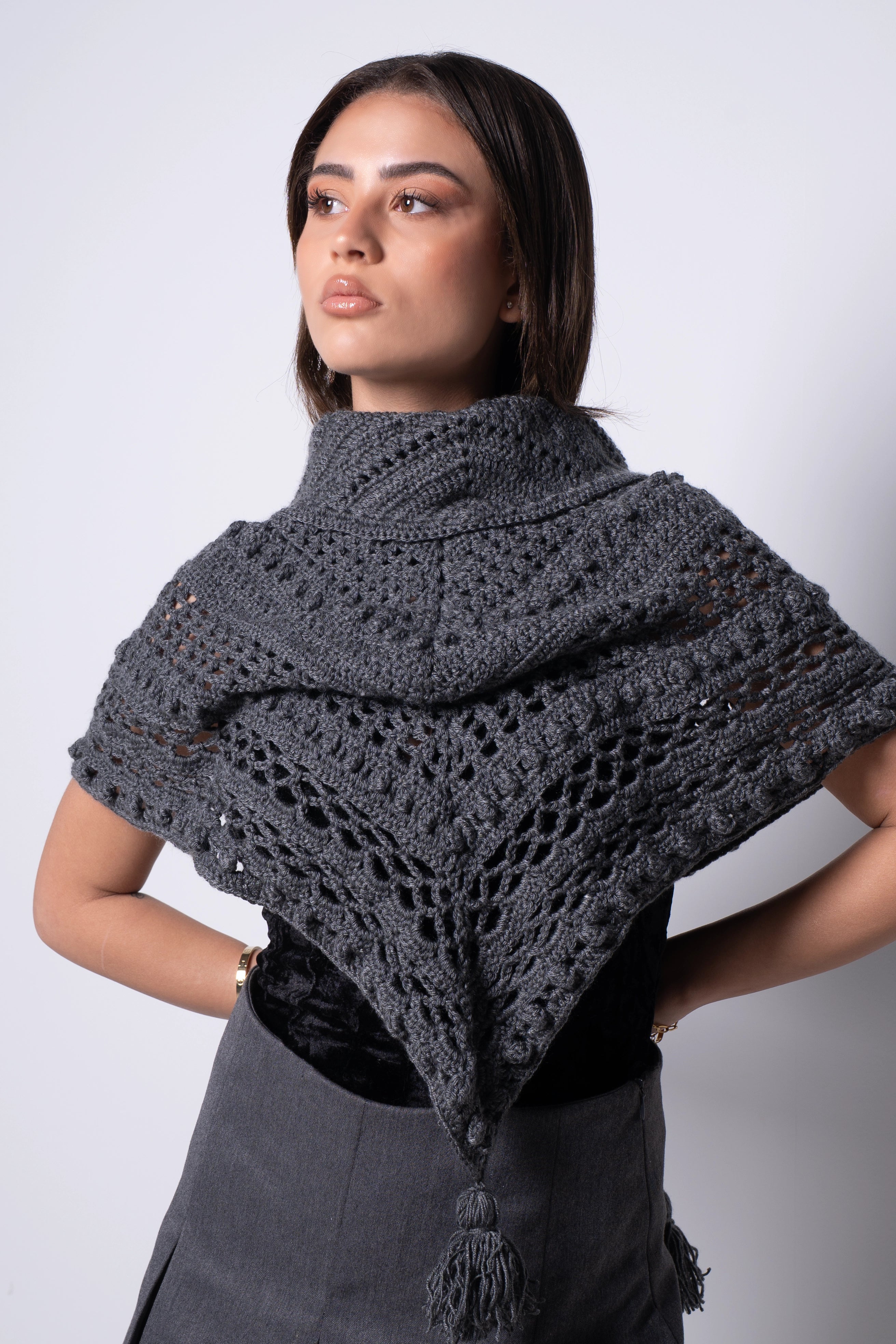 Woman wearing a dark gray knitted shawl against a plain background