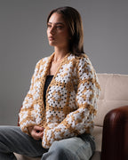 Woman wearing a white and brown crochet cardigan sitting on a couch.