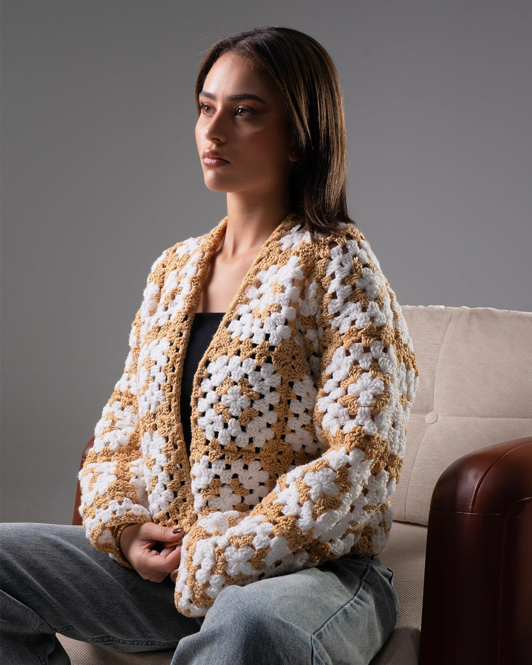 Woman wearing a white and brown crochet cardigan sitting on a couch.