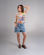 Woman wearing a colorful crochet top and denim shorts on a gray background
