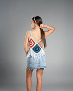 Woman wearing a colorful top with geometric patterns and a denim skirt on a gray background