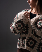 Person wearing a colorful crochet cardigan against a dark background
