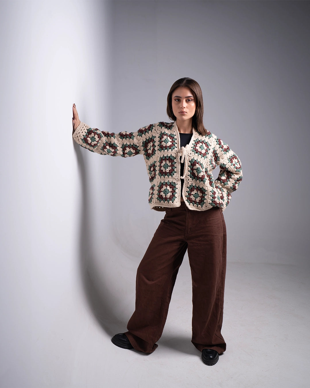 Woman wearing a patterned jacket and brown pants against a plain background