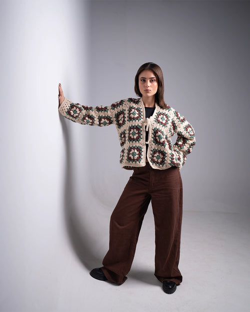 Woman wearing a patterned jacket and brown pants against a plain background