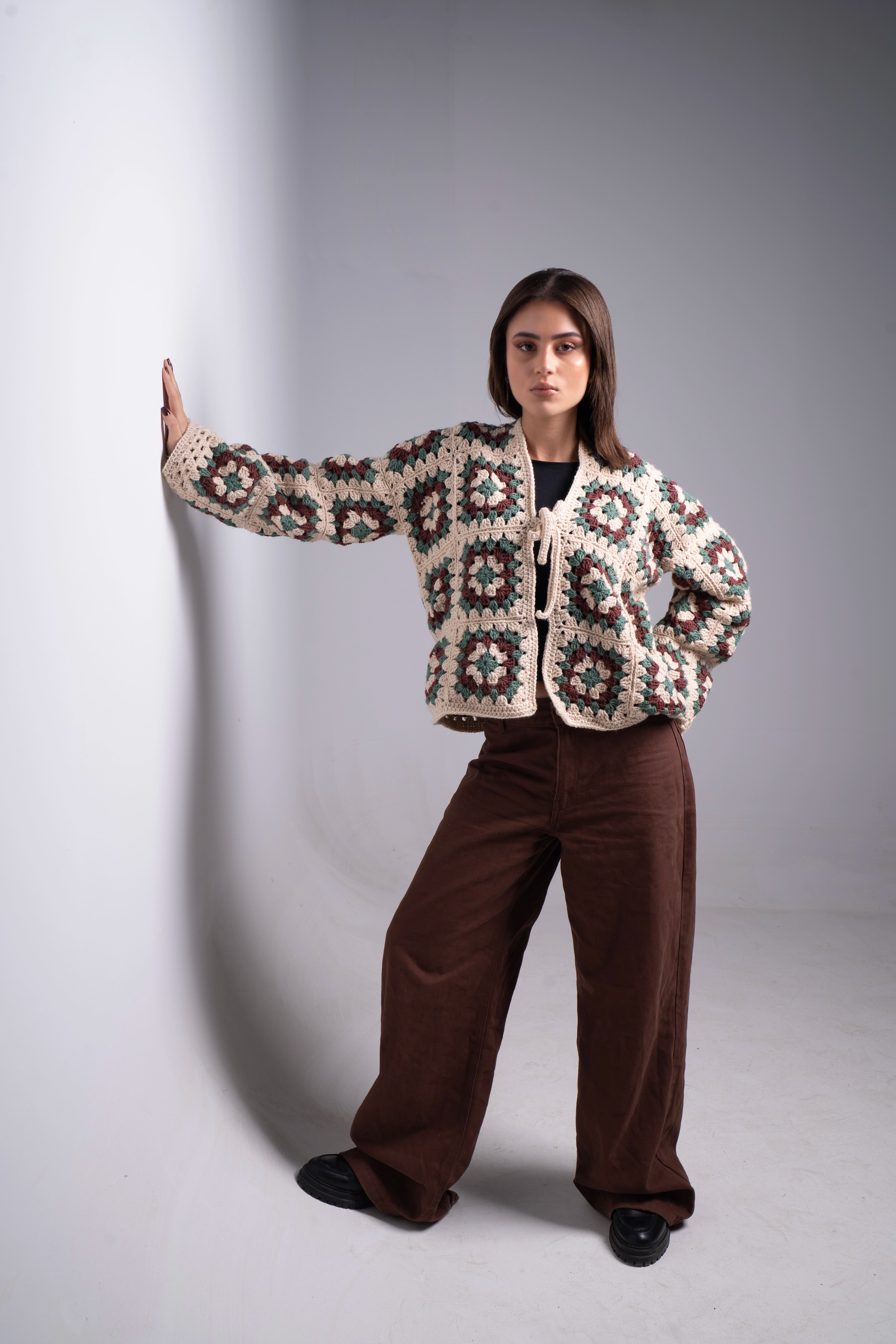 Person wearing a patterned jacket and brown pants against a gray background