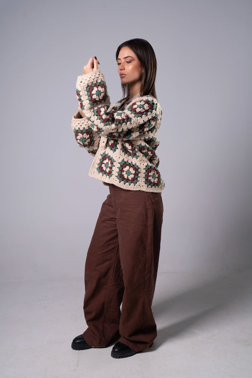 Woman wearing a patterned sweater and brown pants against a gray background