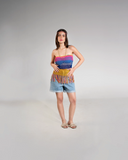Woman wearing a colorful striped top and denim shorts on a gray background