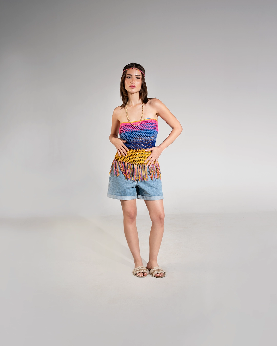 Woman wearing a colorful striped top and denim shorts on a gray background
