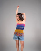 Woman wearing a colorful crochet top and denim shorts on a gray background