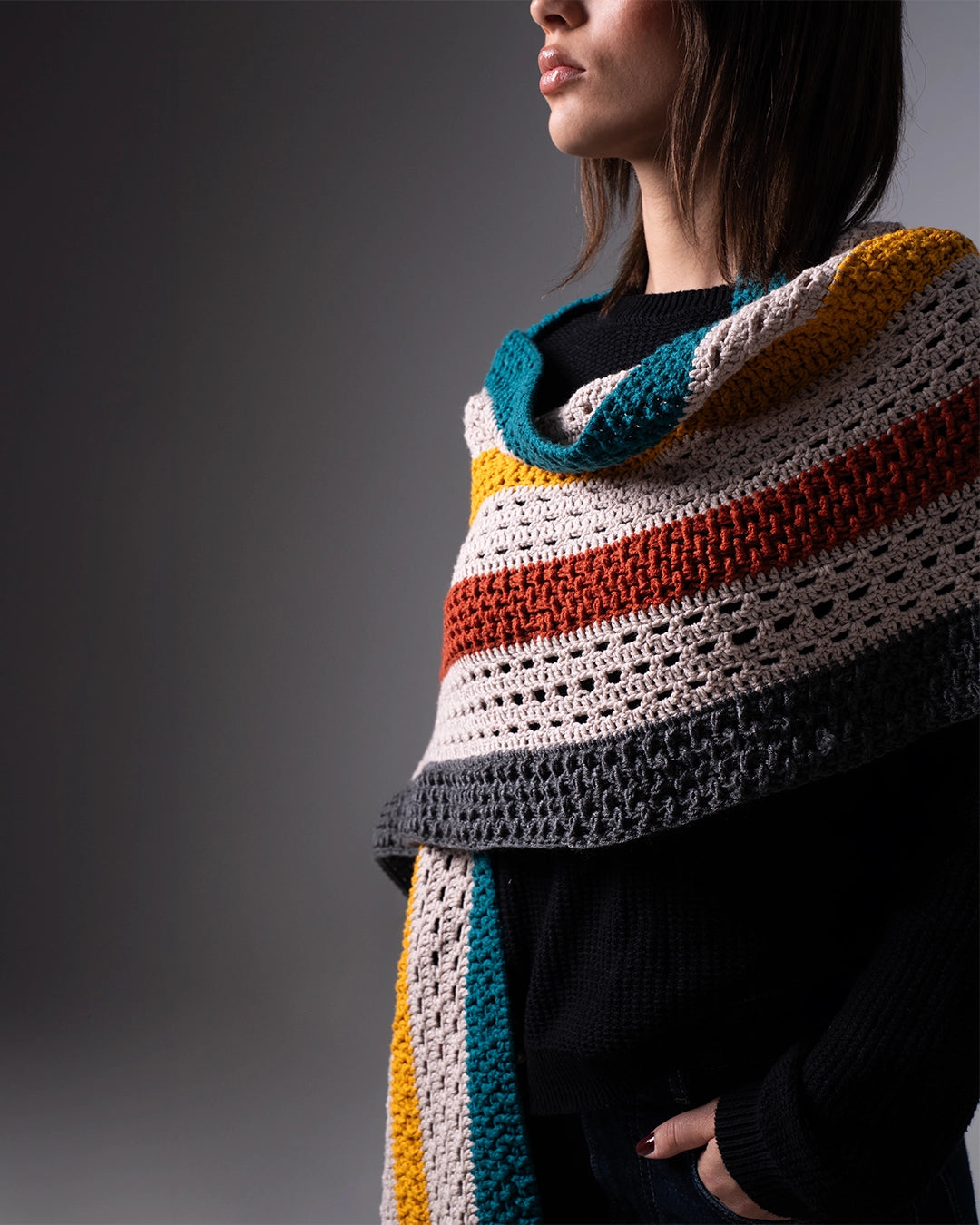 Person wearing a colorful striped crochet shawl on a gray background