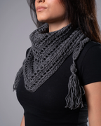 Person wearing a gray knitted scarf with tassels on a gray background