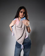 Woman wearing a large knitted shawl with colorful accents on a gray background