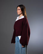 Woman wearing a burgundy sweater over a white shirt with blue jeans on a gray background