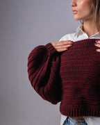 Person wearing a burgundy sweater against a gray background