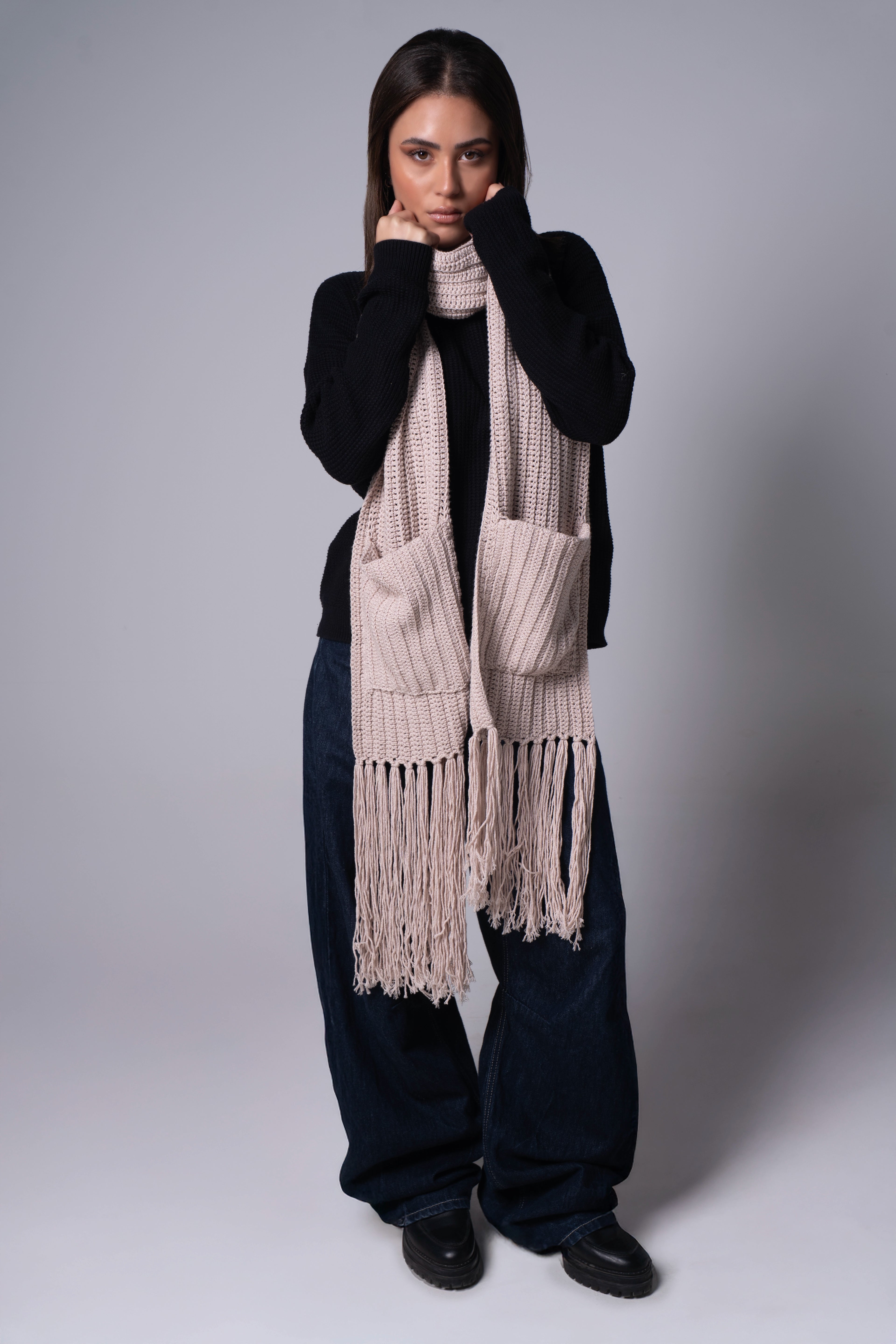 Woman wearing a long beige scarf with fringes on a plain background