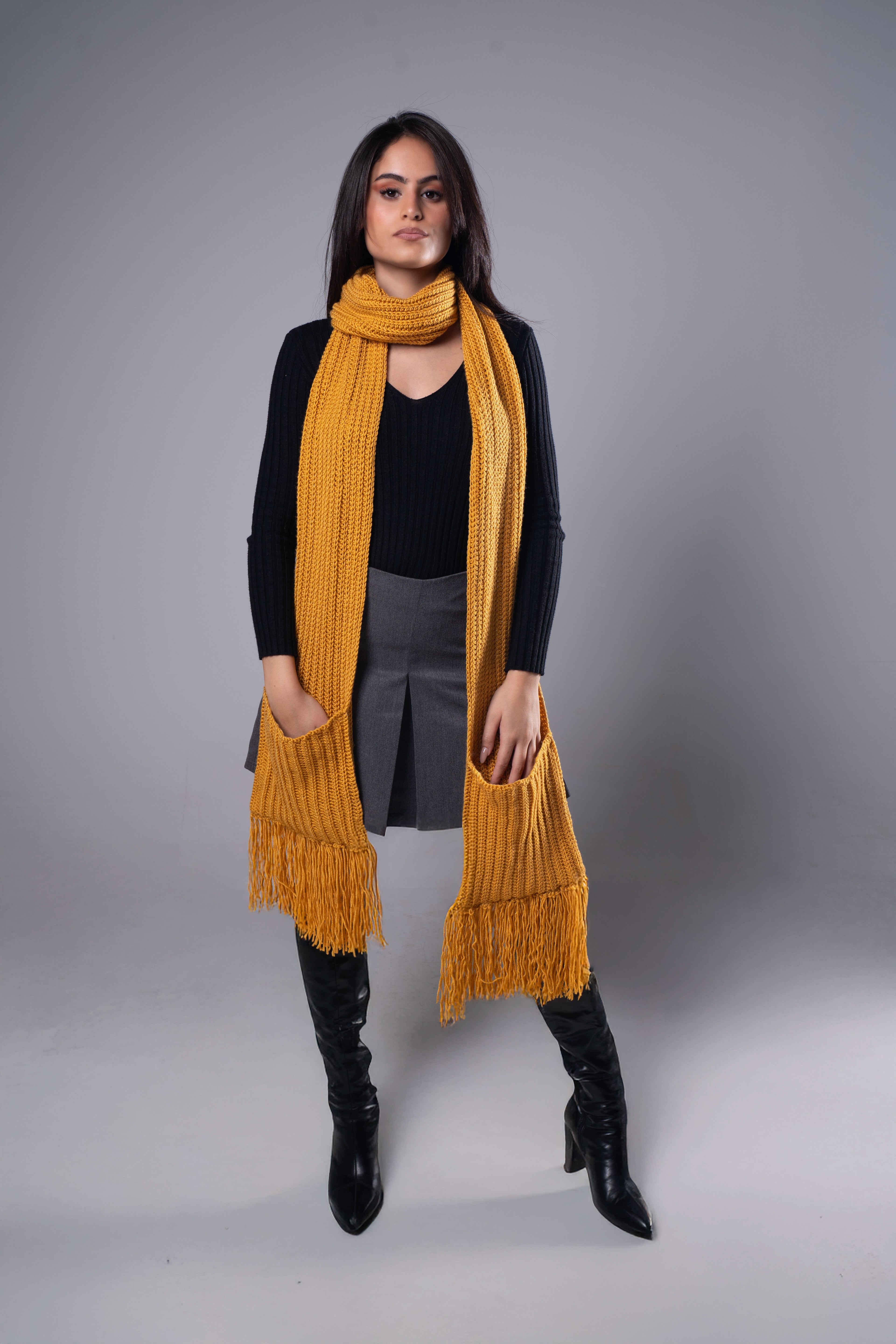 Woman wearing a long mustard yellow scarf with black outfit on a gray background