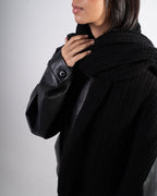 Person wearing a black coat with leather sleeves on a plain background