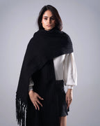 Woman wearing a black knitted shawl with fringes on a gray background