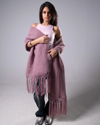 Woman wearing a pink knitted shawl with fringe on a gray background