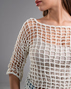 Close-up of a person wearing a white crochet top against a gray background