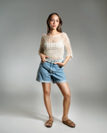 Woman wearing a beige crochet top and blue shorts on a gray background