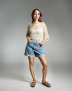 Woman wearing a beige crochet top and blue shorts on a gray background