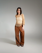 Woman wearing a beige top and brown pants on a gray background
