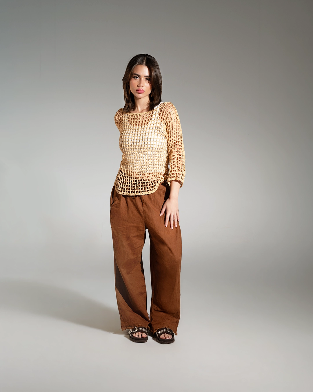 Woman wearing a beige top and brown pants on a gray background