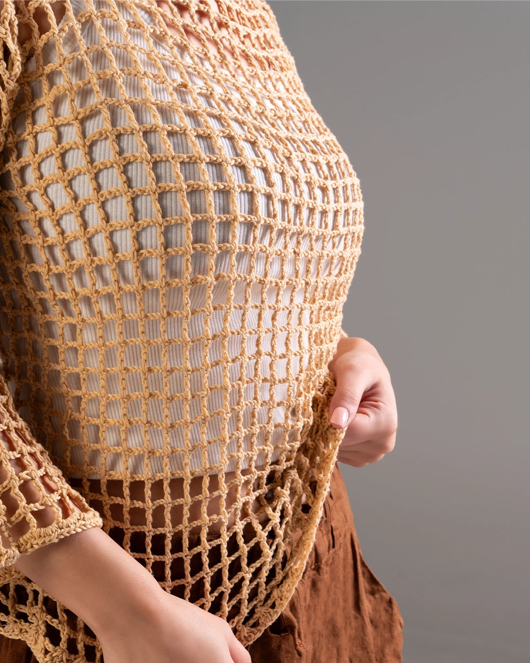 Close-up of a person wearing a bronze crochet top against a gray background