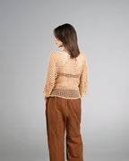 Woman wearing a beige mesh top and brown pants on a gray background