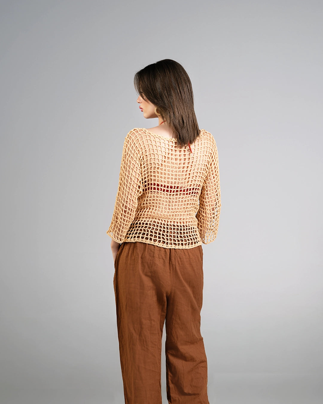 Woman wearing a beige mesh top and brown pants on a gray background