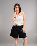 Woman wearing a white crochet top and black shorts on a gray background